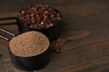 Aromatic clove powder and dried buds in scoops on wooden table, closeup. Space for text