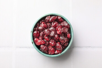 Tasty dried cranberries in bowl on white tiled table, top view