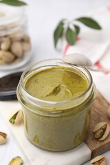 Tasty pistachio cream in jar and nuts on white table, closeup