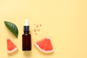 Flat lay composition with grapefruit essential oil on pale yellow background. Space for text