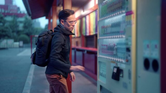 Side view of content Hispanic tourist male with backpack buying snack in vending machine on street in evening during vacation in Tokyo, Japan