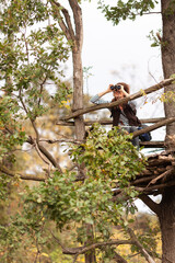 Naklejka na ściany i meble Adult Woman Watching Wildlife from a Tree Observation Platform with Binoculars