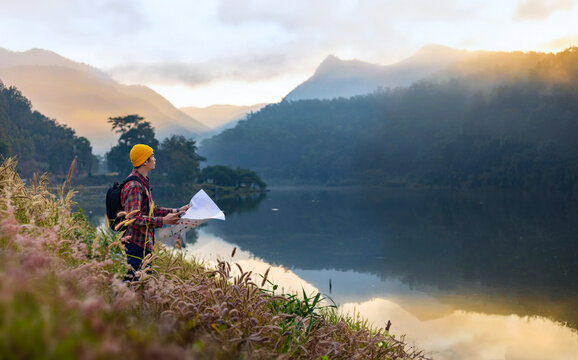 Asian naturalist looking at map for direction while exploring wildlife in the forest by the lake for surveying and discovering the rare biological diversity and ecologist on the field study in autumn