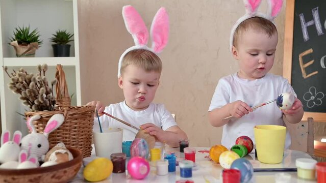 Two children with bunny ears funny painting Easter eggs at home