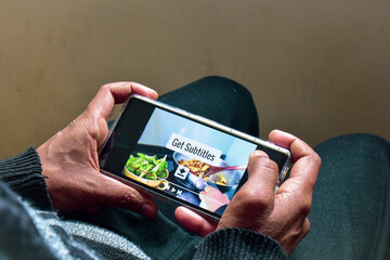 Man watching a cooking recipe video on his smartphone with the message Get Subtitles. Download...