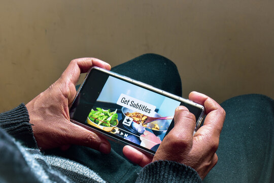 Man watching a cooking recipe video on his smartphone with the message Get Subtitles. Download Subtitles for foreign language translation, selective focus.