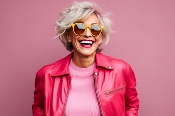 Portrait of a happy senior woman in pink jacket and sunglasses over pink background