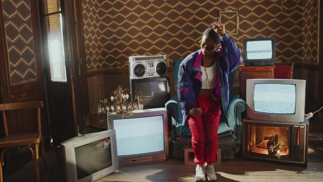 Expressive Black girl in 80s shell suit dancing rhythmically in retro-styled room with noisy analog TVs, cassette tape player and vintage chandelier decor