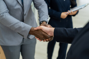 Closeup of business hands shaking between businessman and professional male leader while smart businesswoman stand near at modern office corridor. Represented unity, corporate, teamwork. Ornamented.