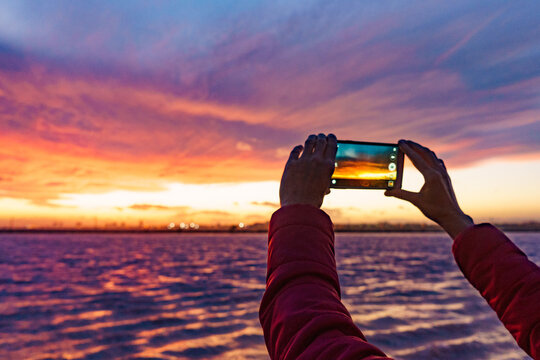 Hand photographing seascape at sunset with mobile phone