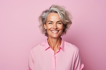 Portrait of smiling senior woman in pink shirt on pink background. - obrazy, fototapety, plakaty