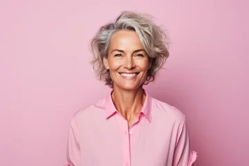 Foto op Canvas Portrait of smiling senior woman in pink shirt on pink background. © Inigo