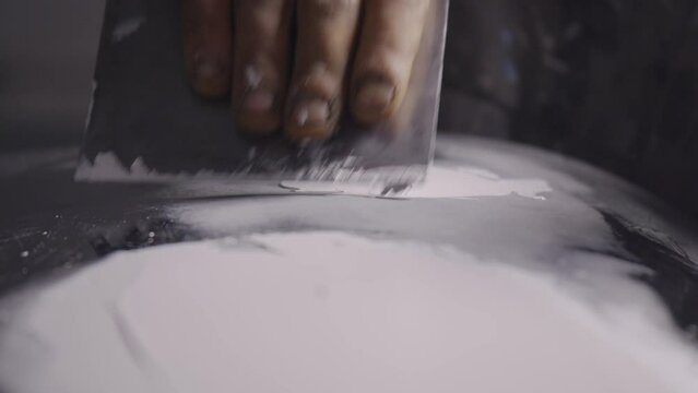 Auto body specialist repairer carefully applies putty to car bodywork CLOSE UP