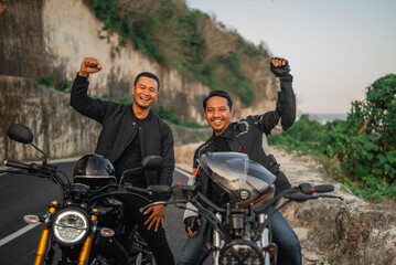 Fototapeta na wymiar asian riders sitting on motorbike with raised fist pump celebration gesture