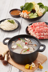 top view shot of a Chinese hot pot on a white wooden table with beef mushrooms, chili, 