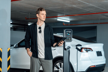 Young man travel with EV electric car to shopping center parking lot charging in downtown city...