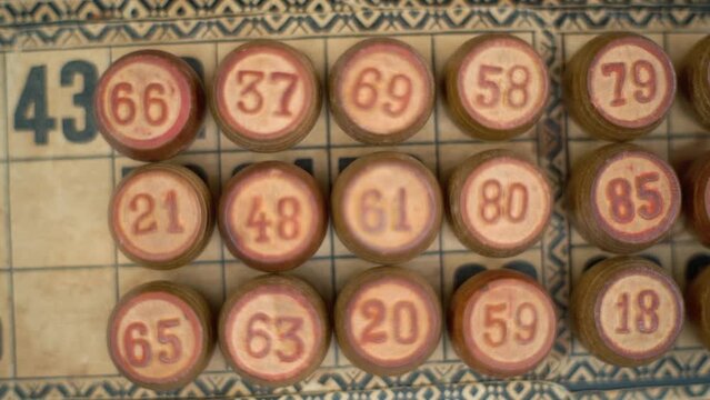 Cinematic close-up smooth zoom out shot of a Bingo wooden barrels, woody figures, on a old numbers textured background, vintage board game, professional lighting, slow motion 120 fps