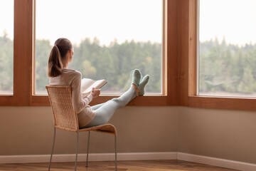 woman looking out window reading book enjoying relaxing time at home 