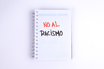 photograph of notebook with phrase "stop racism" in spanish on a white background.
