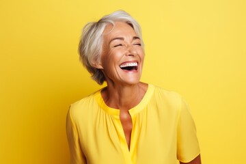 Obraz na płótnie Canvas Portrait of happy senior woman laughing and looking up against yellow background