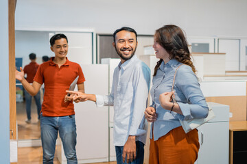 Asian couple chooses a wooden cabinet while shopping served by a male waiter at a furniture store