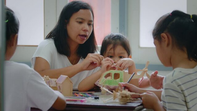 Asian girl and her older sister are coloring on a assembly wooden toy