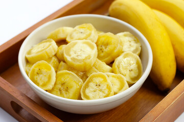 Naklejka na ściany i meble Banana slices in white bowl on wooden tray.