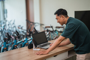 male shop assistant stands while working with laptop computer in bicycle shop