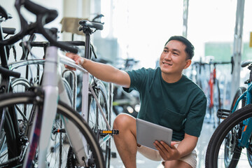 young male employee using a tablet while checking a bicycle frame at a bicycle shop