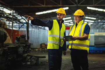 Warehouse and factory workers in uniform, wearing yellow hard hats and safety helmets, collaborate...