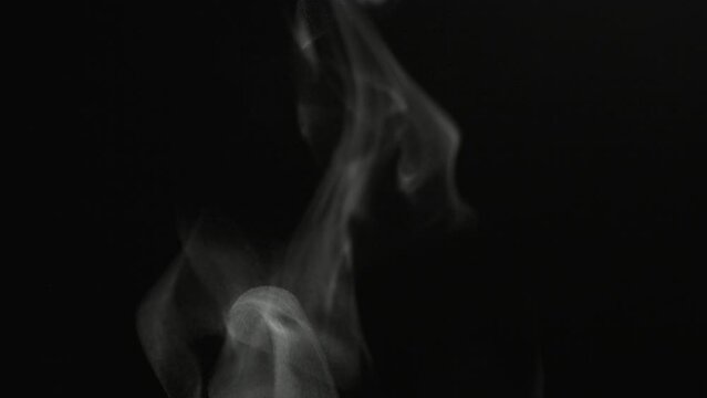 Close up steam particles swirling and rising on a black background in slow motion