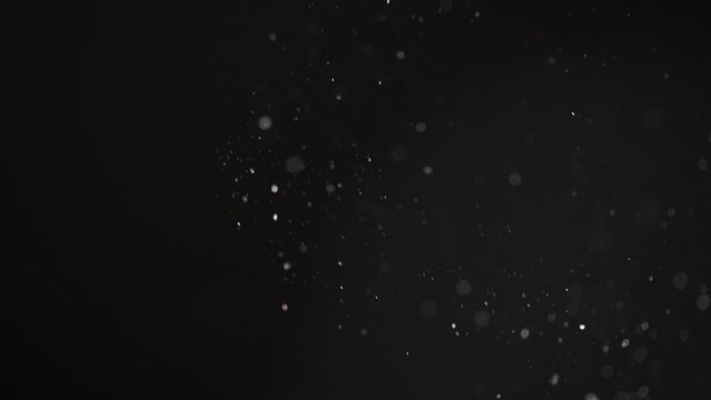 Abstract macro particles floating upwards on a black background in slow motion