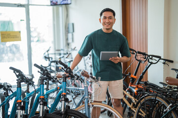 Fototapeta na wymiar entrepreneurial man stands smiling at the camera holding a digital tablet in a bicycle shop
