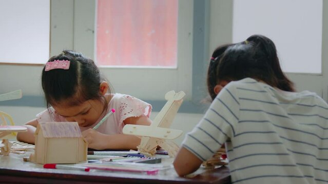 Asian girl and her older sister are coloring on assembly wooden toy