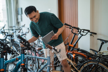 young man looks at the new model of a bicycle while using a tablet at a bicycle shop