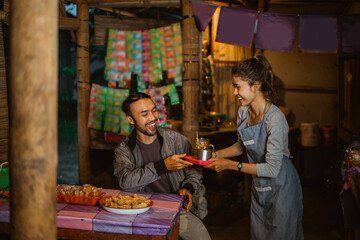 male customers are happy when a female stallholder gives them a drink at a traditional stall