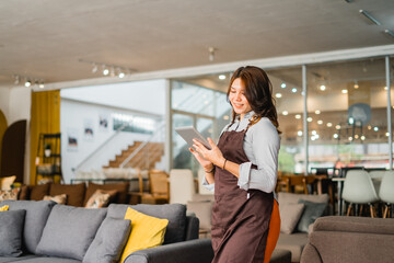 female waitress in apron using a tab standing in front of couch in furniture store department