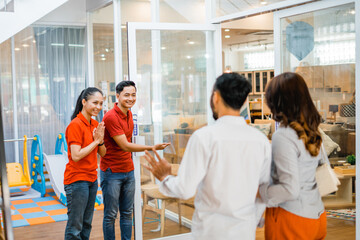 two shop assistants in red greet with a welcome hand gesture when customers come to the furniture...
