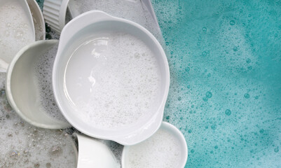 Fototapeta na wymiar Plates and bowl soaking in foam of dishwashing liquid
