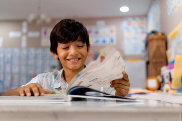 Portrait of elementary boy reading a book in a class.