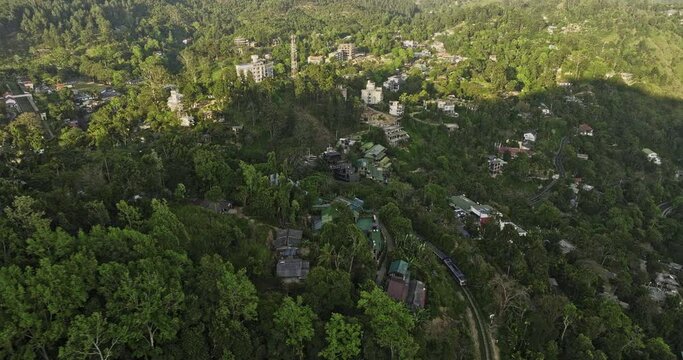 Ella Sri Lanka Aerial v5 birds eye view drone follows the train winding through verdant hills, entering railway station capturing hillside resort hotels at sunset - Shot with Mavic 3 Cine - April 2023