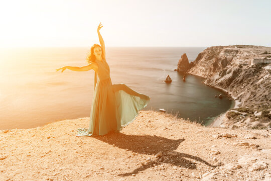 Woman green dress sea. Female dancer posing on a rocky outcrop high above the sea. Girl on the nature on blue sky background. Fashion photo.
