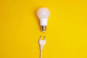 Light bulb and electrical plug on yellow background. Concept of saving energy by using LED lamp - obrazy, fototapety, plakaty