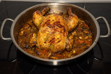 Whole chicken on a bed of vegetables fresh from the oven in a steel pan.  Close-up