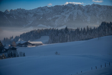 Beautiful winter landscape.  Some idyllic farmhouses in front of the Zahmer Kaiser mountain range...