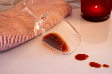 Chipped wine glass on a white table.  A few spilled drops of wine, red and white cloth and red...
