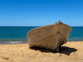 Fototapeta na wymiar Small metal boat on a golden sand beach with blue water and waves under a blue sky.