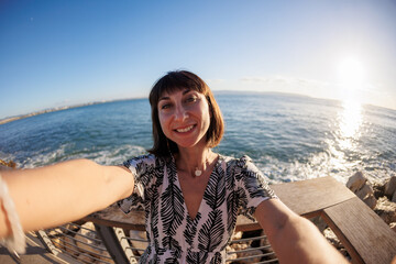 A young and cheerful girl in a dress takes a selfie on the beach.