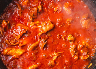 Chicken meat is stewed in tomato in a frying pan