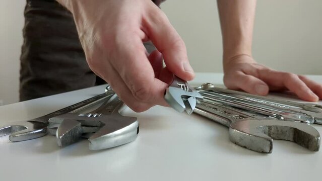 Man choosing small adjustable wrench, multiple spanners on worktop